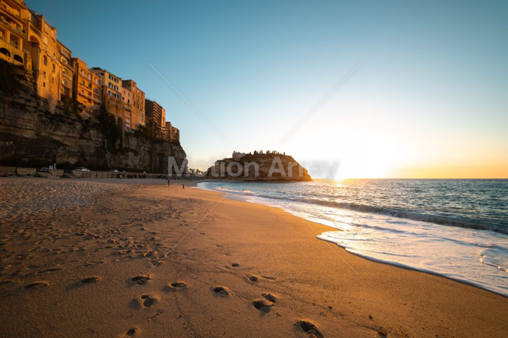 Footprints in the sand along a beack with buildings on a cliff face in the distance